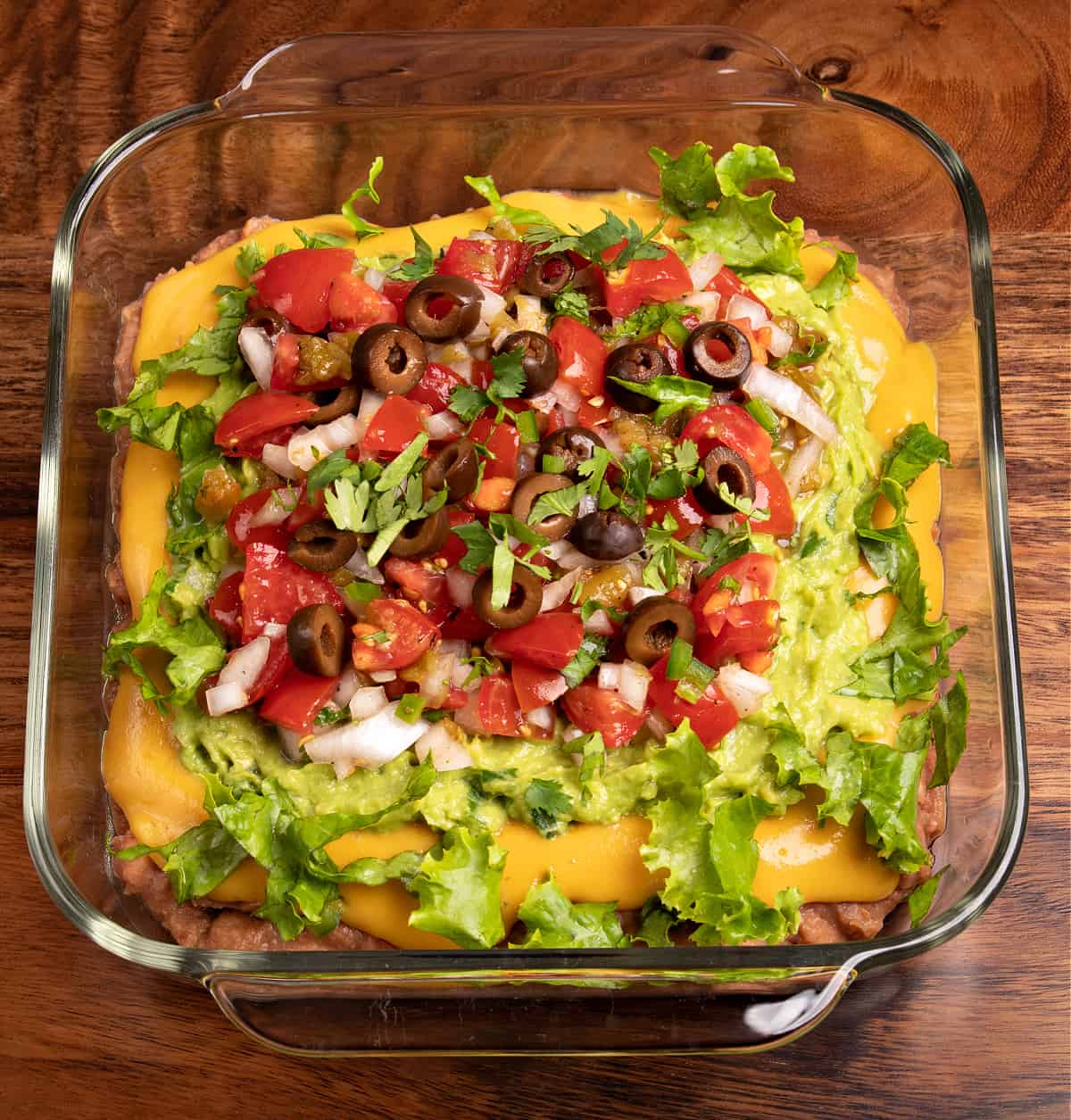 Top down photo of my 7 layer dip topped with homemade Pico De Gallo, black olives, shredded lettuce, and cilantro