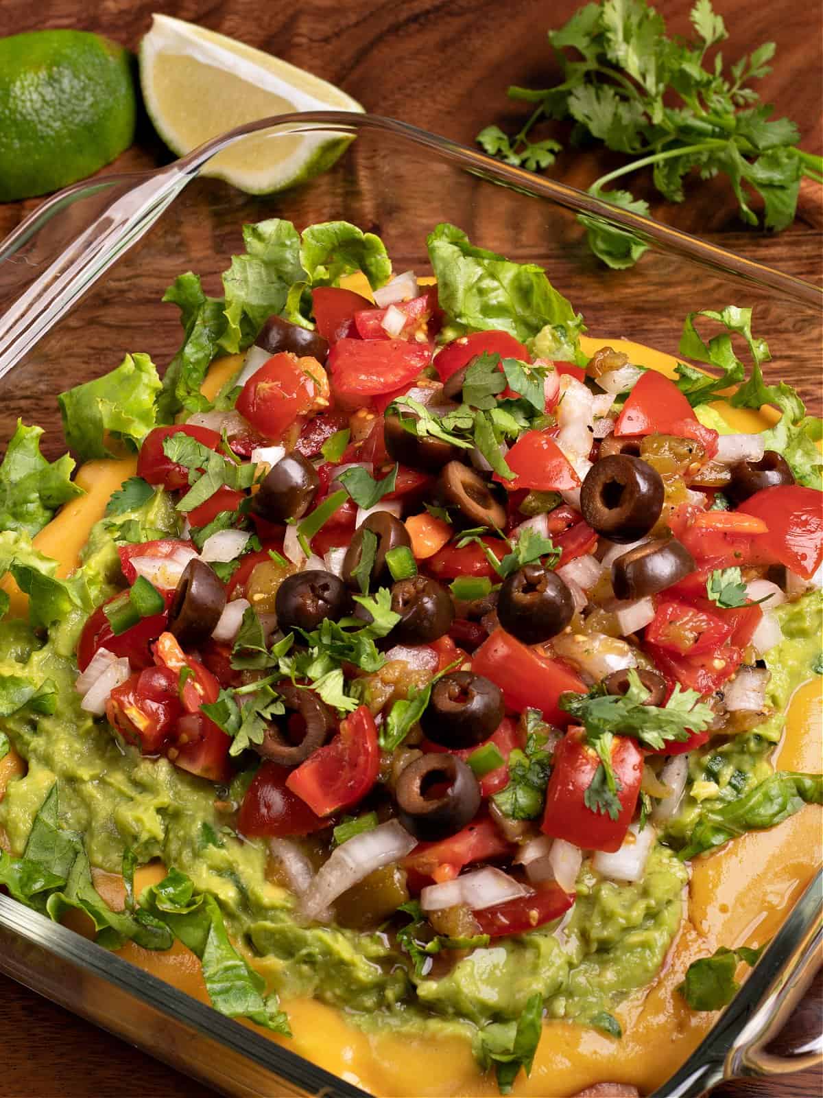 picture of my vegan 7 layer dip in a square, glass casserole dish with garnishes of cilantro and lime