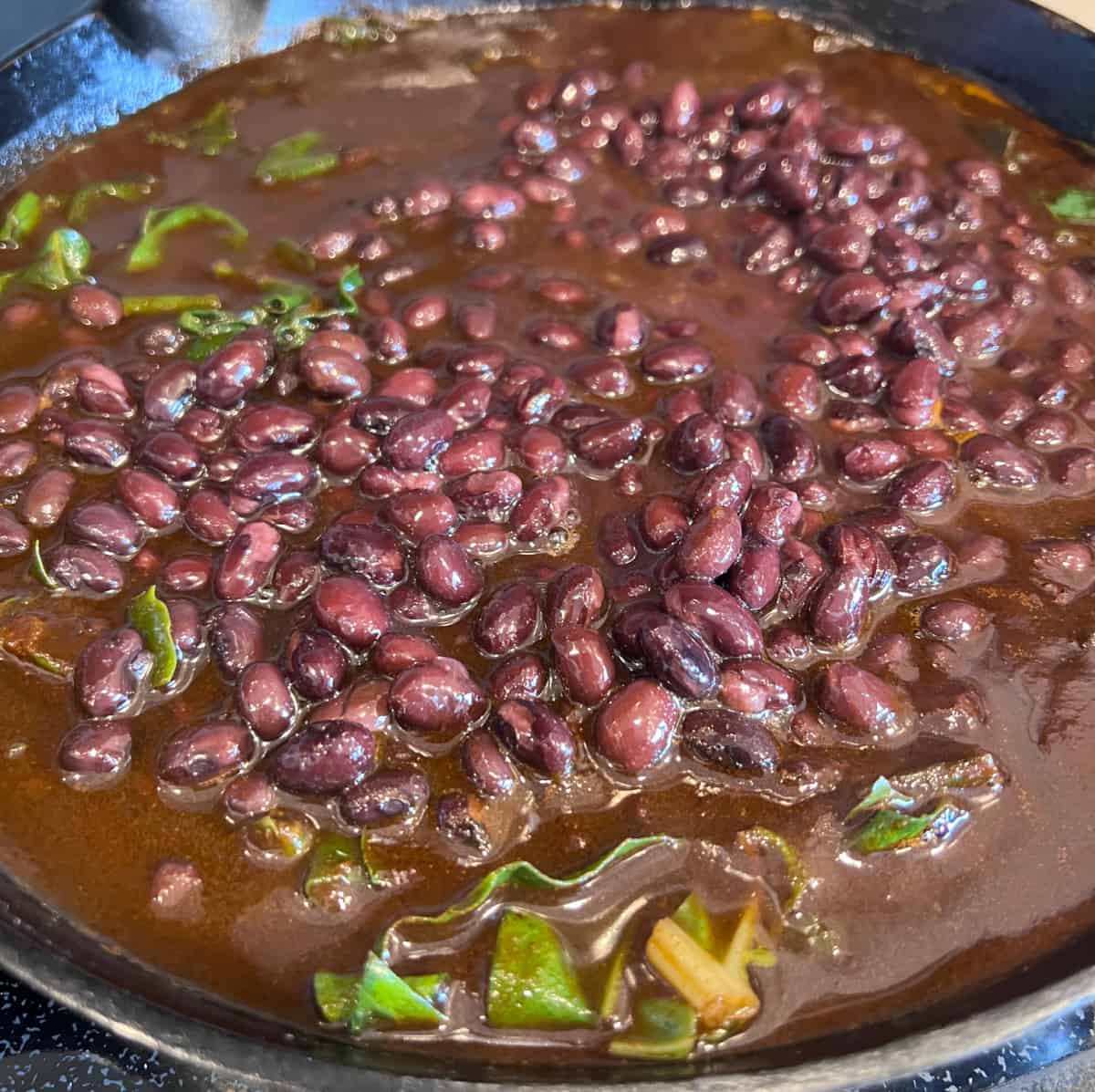 skillet full of black beans and Swiss chard in a red Chile sauce