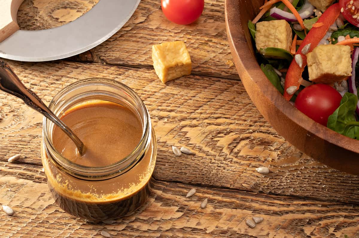 a jar of last minute asian salad dressing next to an ulu knife and a bowl of salad