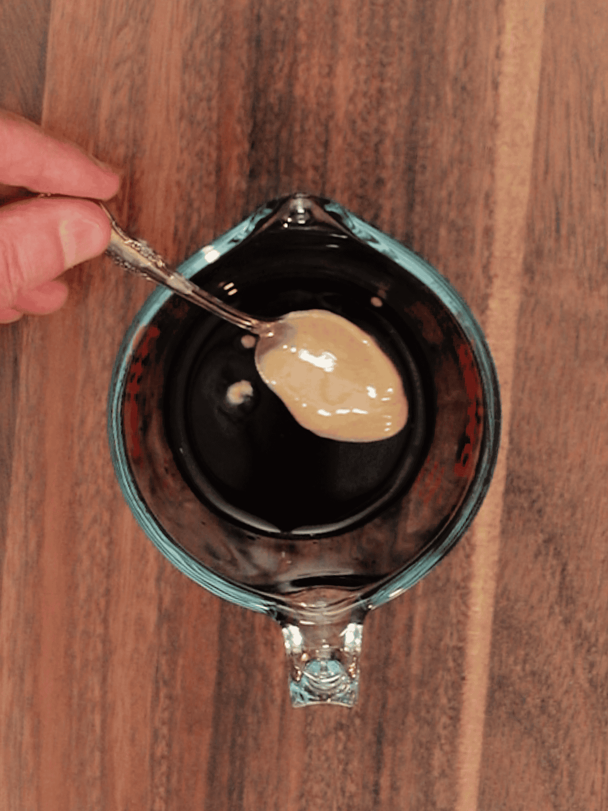adding tahini to a measuring cup with tamari and rice vinegar
