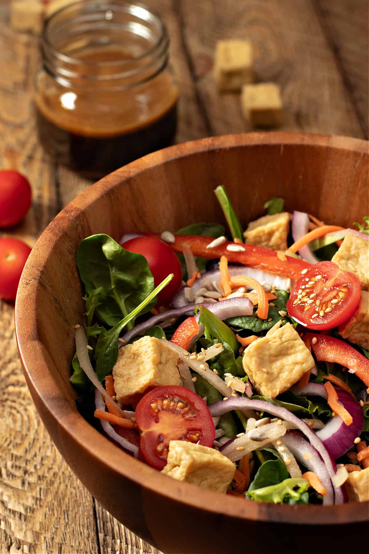 a big wooden bowl of healthy salad with tofu cubes and a jar of my last minute asian salad dressing
