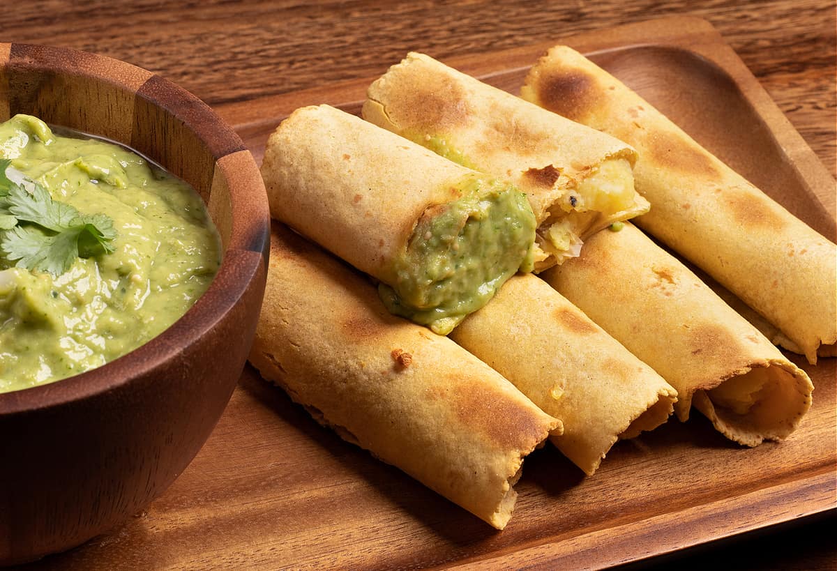 Horizontal photo of my mashed potato taquitos and a bowl of my tomatillo avocado salsa