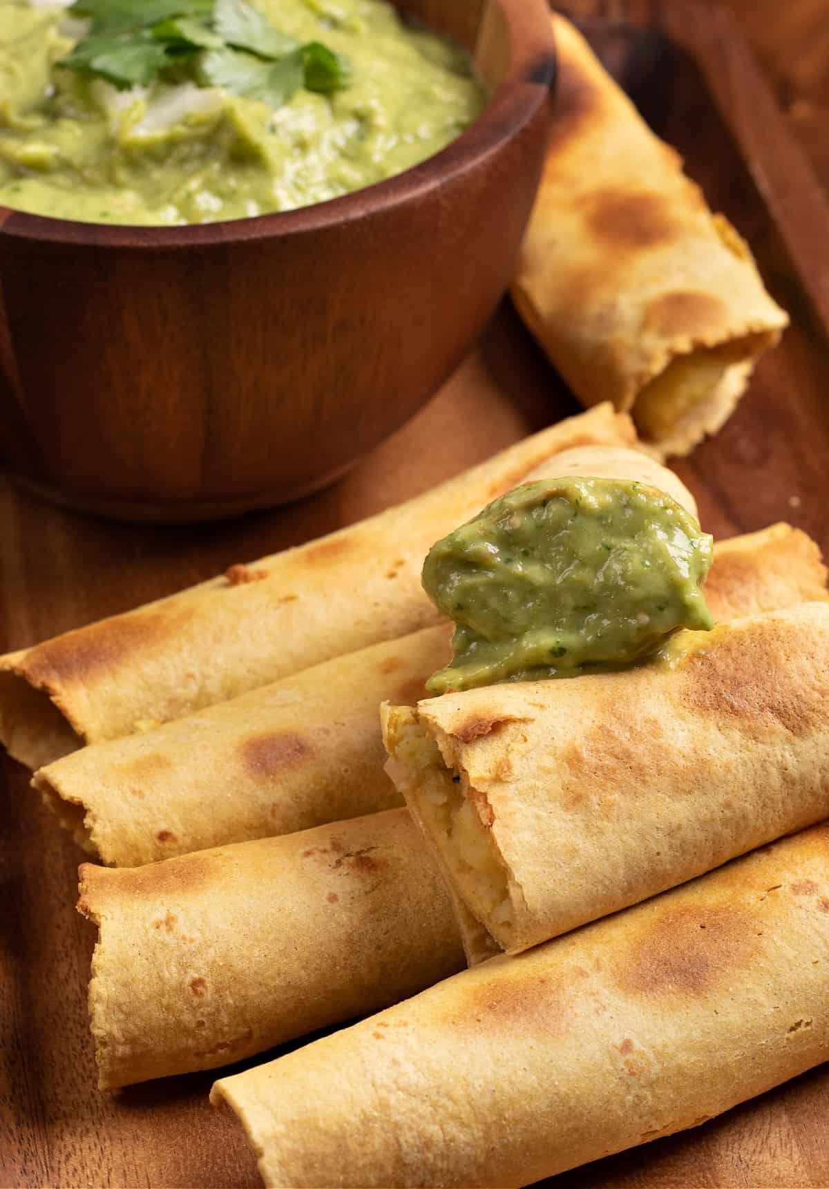 A tray of mashed potato taquitos with a bowl of tomatillo avocado salsa to dip in
