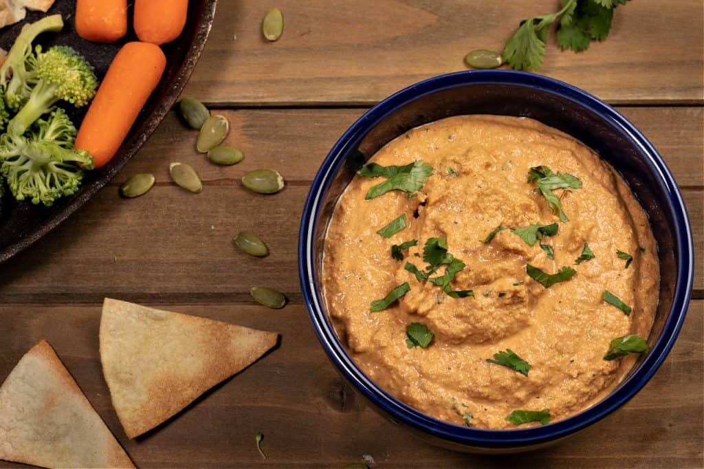 horizontal image of fresh veggies, homemade corn chips, and a bowl of roasted pumpkin seed dip