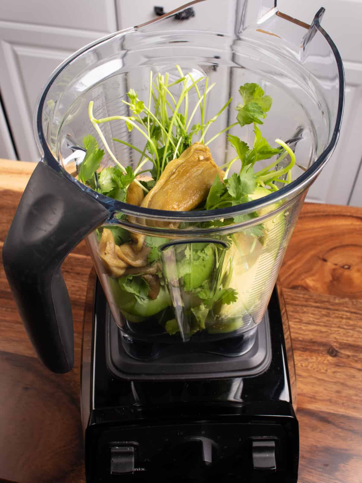 Blender jar full of the ingredients to make tomatillo avocado salsa