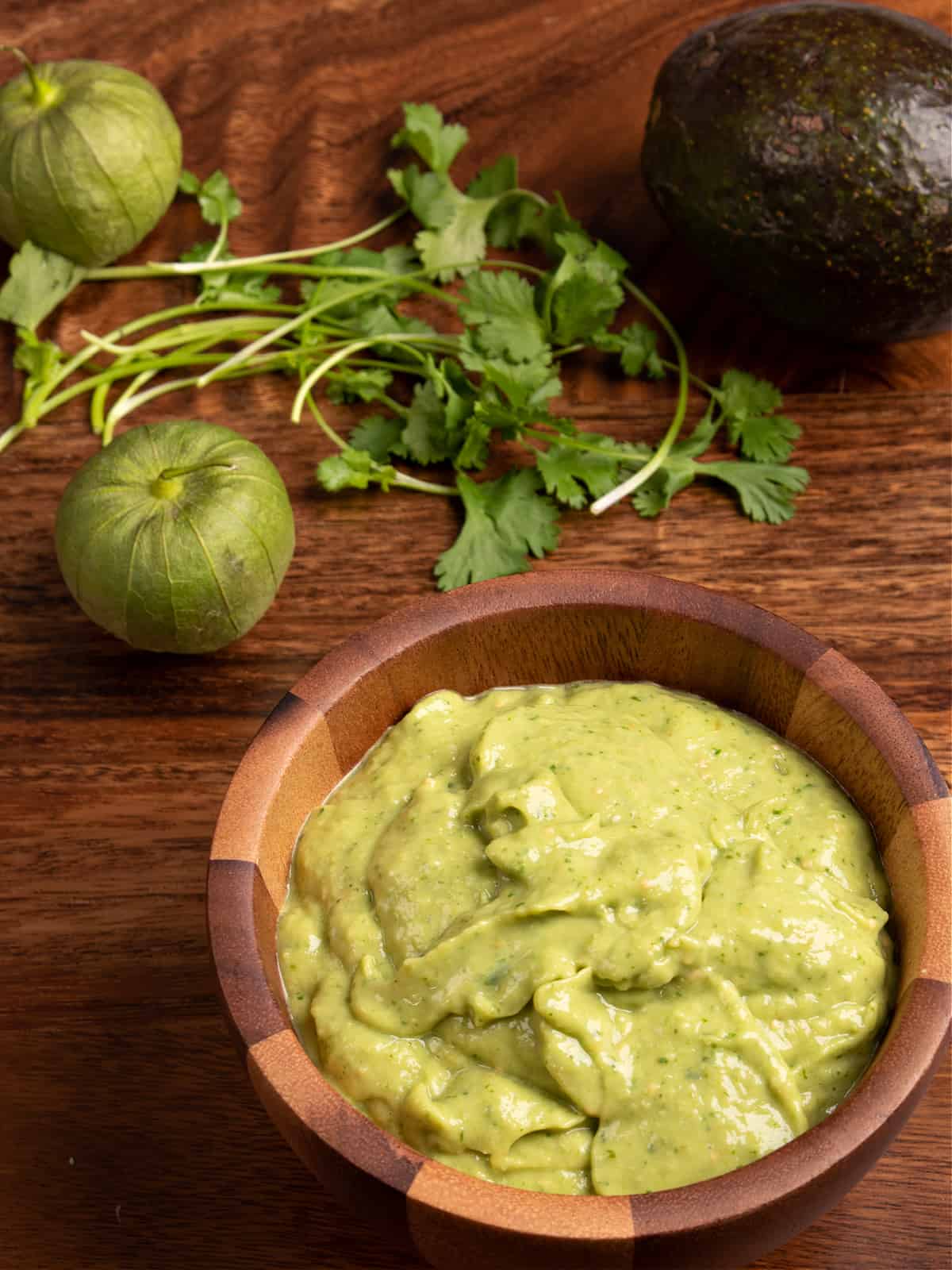 wooden bowl of tomatillo avocado salsa surrounded by raw tomatillos and cilantro