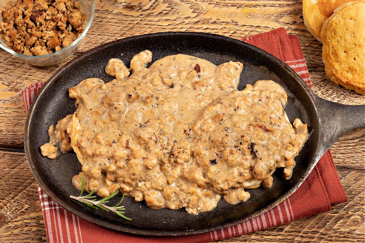 a cup of vegan tofu sausage crumbles, a biscuit, and a plate of vegan biscuits and gravy