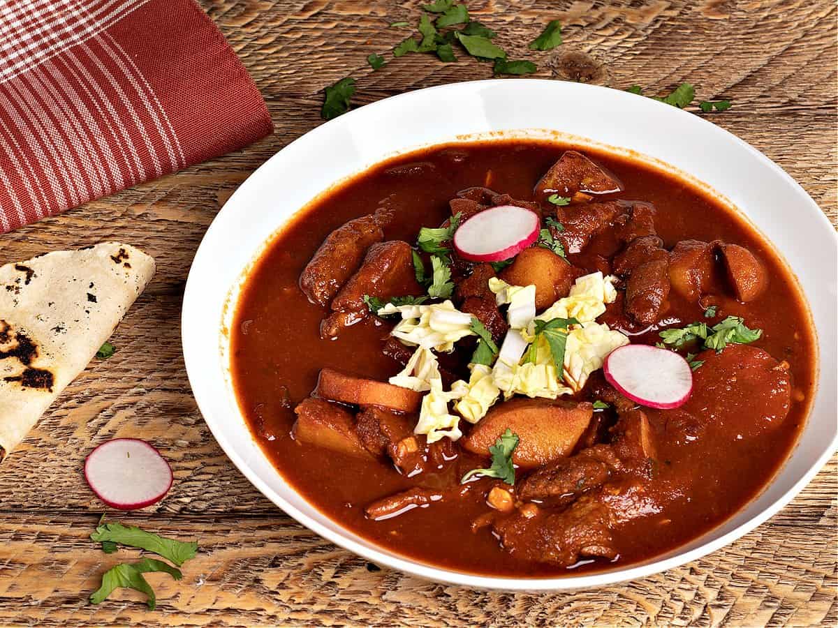 A big bowl of my vegan Chile Colorado garnished with cabbage, radishes, cilantro, and corn tortillas