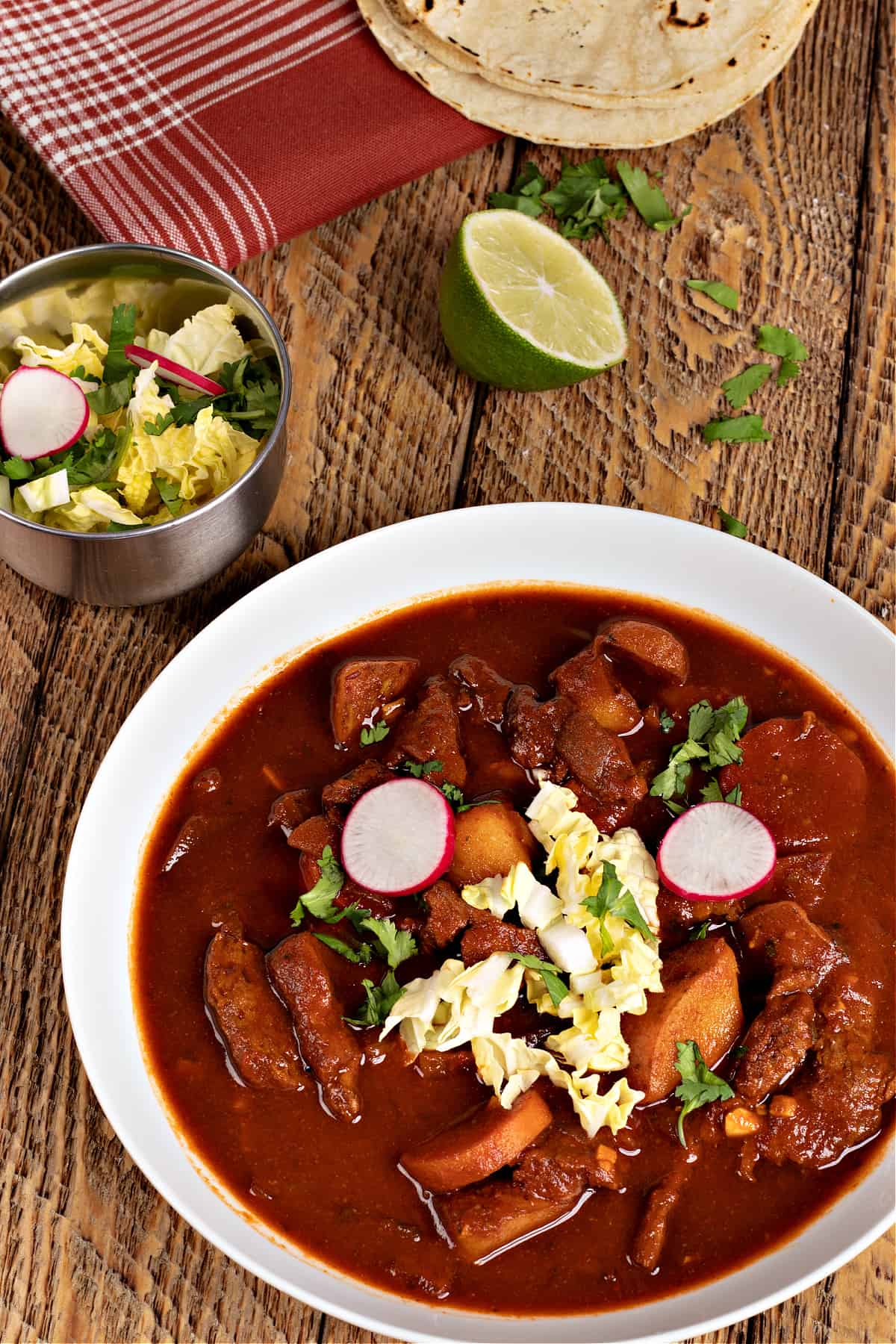 A big bowl of my vegan Chile Colorado garnished with cabbage, radishes, cilantro, and corn tortillas