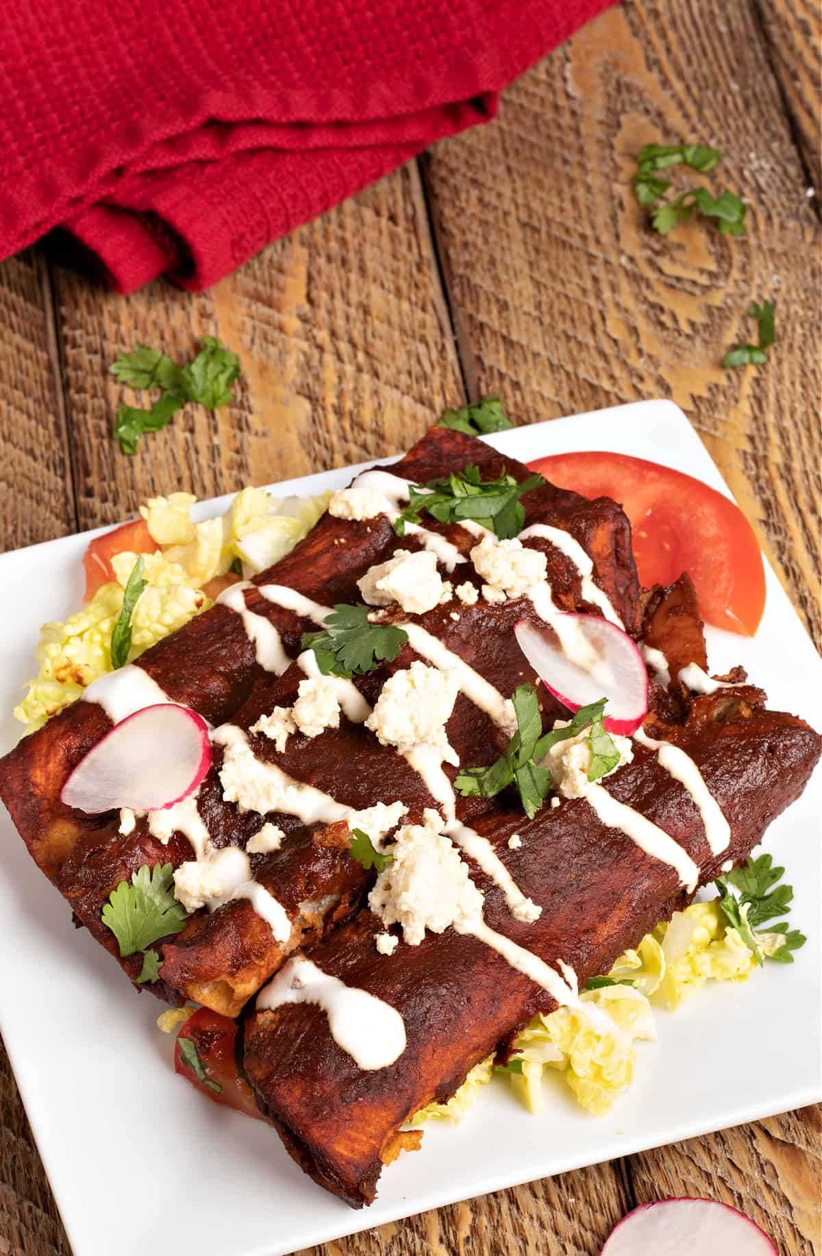 vertical photo of 3 vegan enchiladas mineral sitting on a bed of cabbage slaw and topped with vegan queso fresco and vegan crema