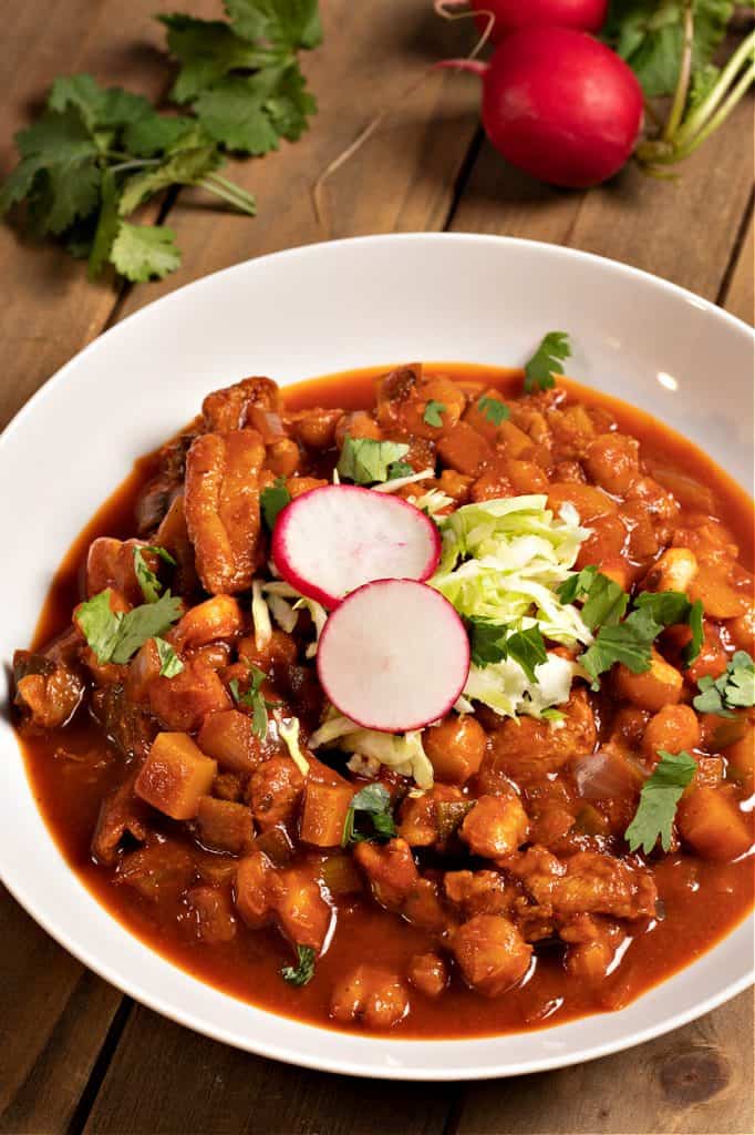 vertical photo of vegan Posole topped with cabbage and radishes